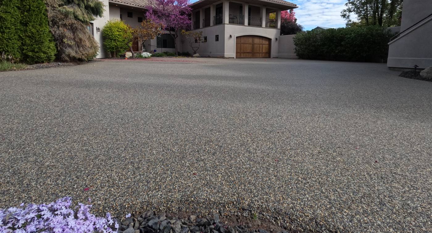 Resin bound driveway in a warm grey stone blend in front of a stucco home